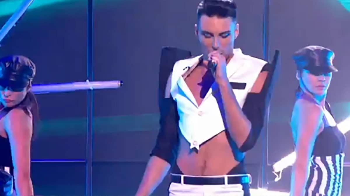 Rylan Clark on stage in singing in 2012 with two women dancing with him - cloths in black and white.