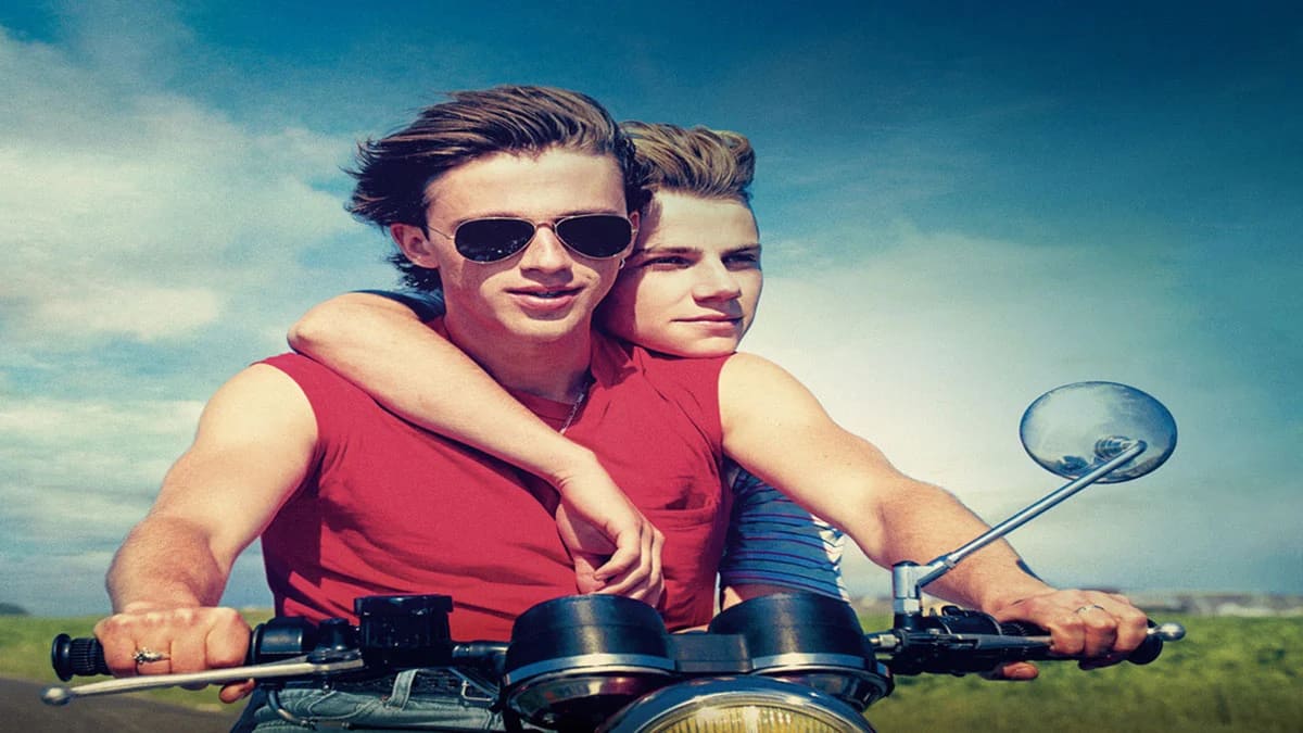 Summer of 85 - two main characters has sleeveless shirts, sitting on motorcycle - driver David played by Benjamin Voisin has red shirt and sunglasses, Alexis played by Félix Lefebvre sitting behind and has one hand over David shoulder to his chest.