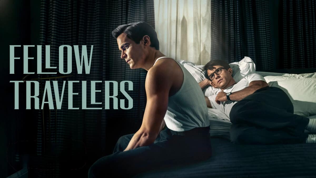 Fellow Travelers - Matt Bomer sitting in bed with a tank top and Jonathan Bailey lay on bed in t-shirt and trousers.